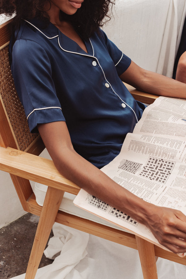 Our model wearing Eva Navy Silk Pyjama Set while sitting on a rattan chair and reading newspaper
